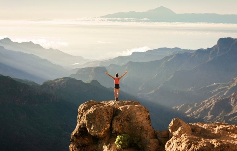 A young girl standing on top of a large rock overlooking at Teide volcano at Nublo Rural Park, Grand Canary, Canary Islands, Spain
